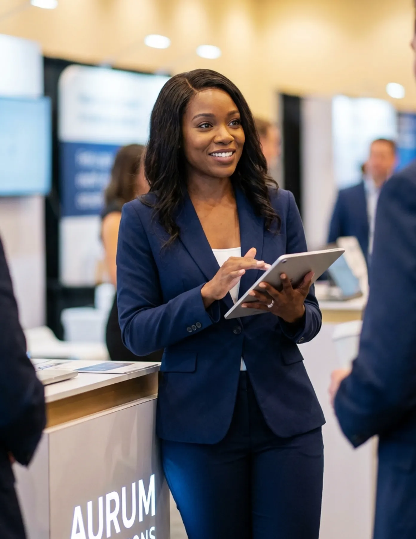 female-event-staff-tablet-corporate-conference-booth-hmg-plus. Professional conference staff member using a tablet to assist attendees at a trade show or corporate event booth