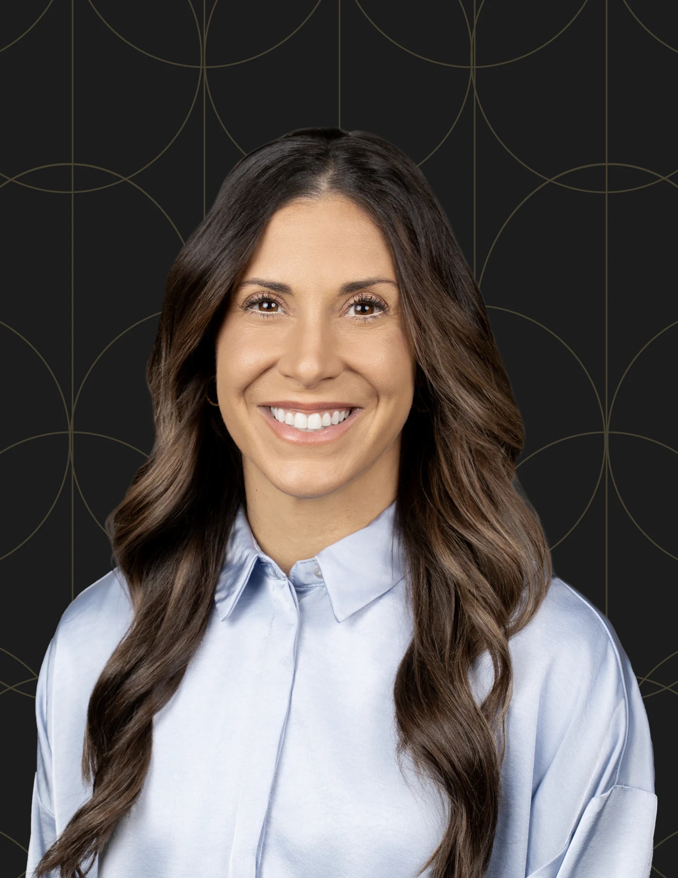 hmg-plus-team-member-headshot-brunette-blue-satin-shirt-hmg-plus. Professional headshot of a woman with long wavy dark brown hair wearing a light blue satin shirt.