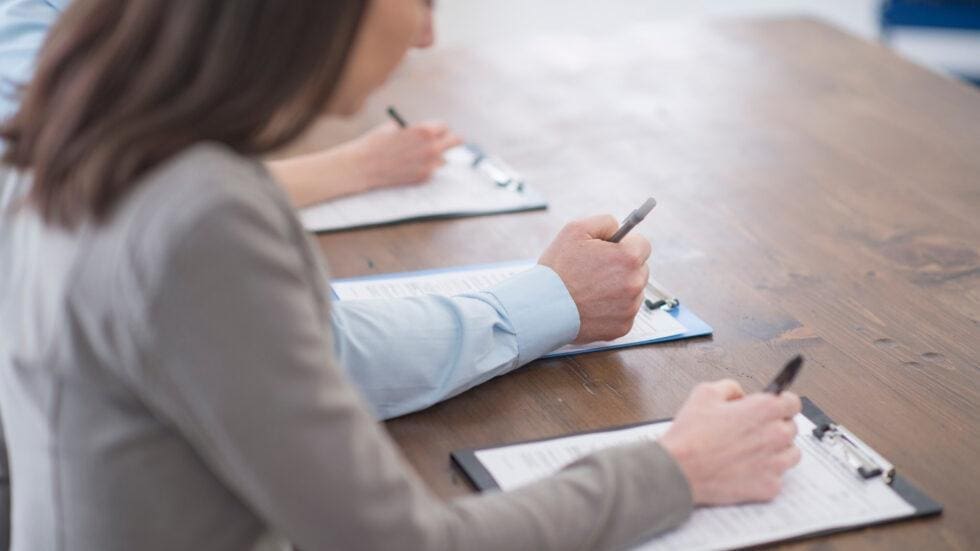 close-up-of-three-people-filling-out-paperwork-on-clipboards-hmg-plus Hospitality professionals completing paperwork during a professional staff vetting and recruitment assessment process at HMG+
